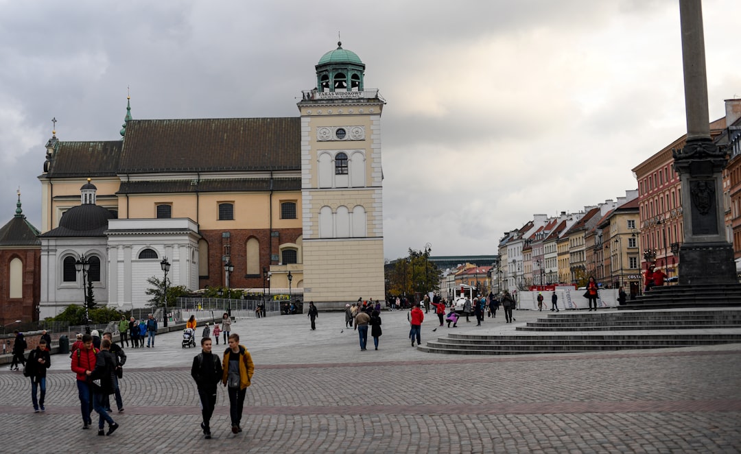 People walk through a european city square with buildings.
